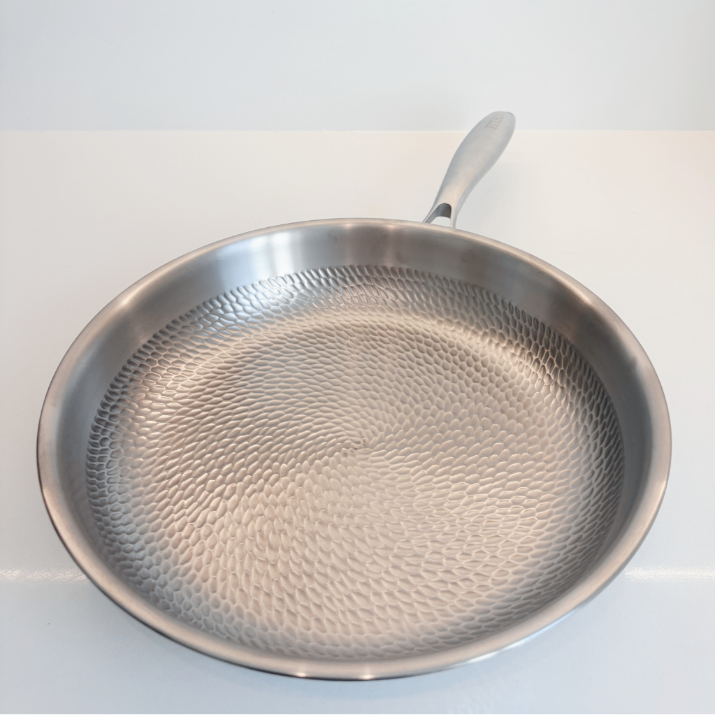 A titanium frying pan with a hammered texture on the inside and a silver handle, photographed on a clean white surface against a white background.