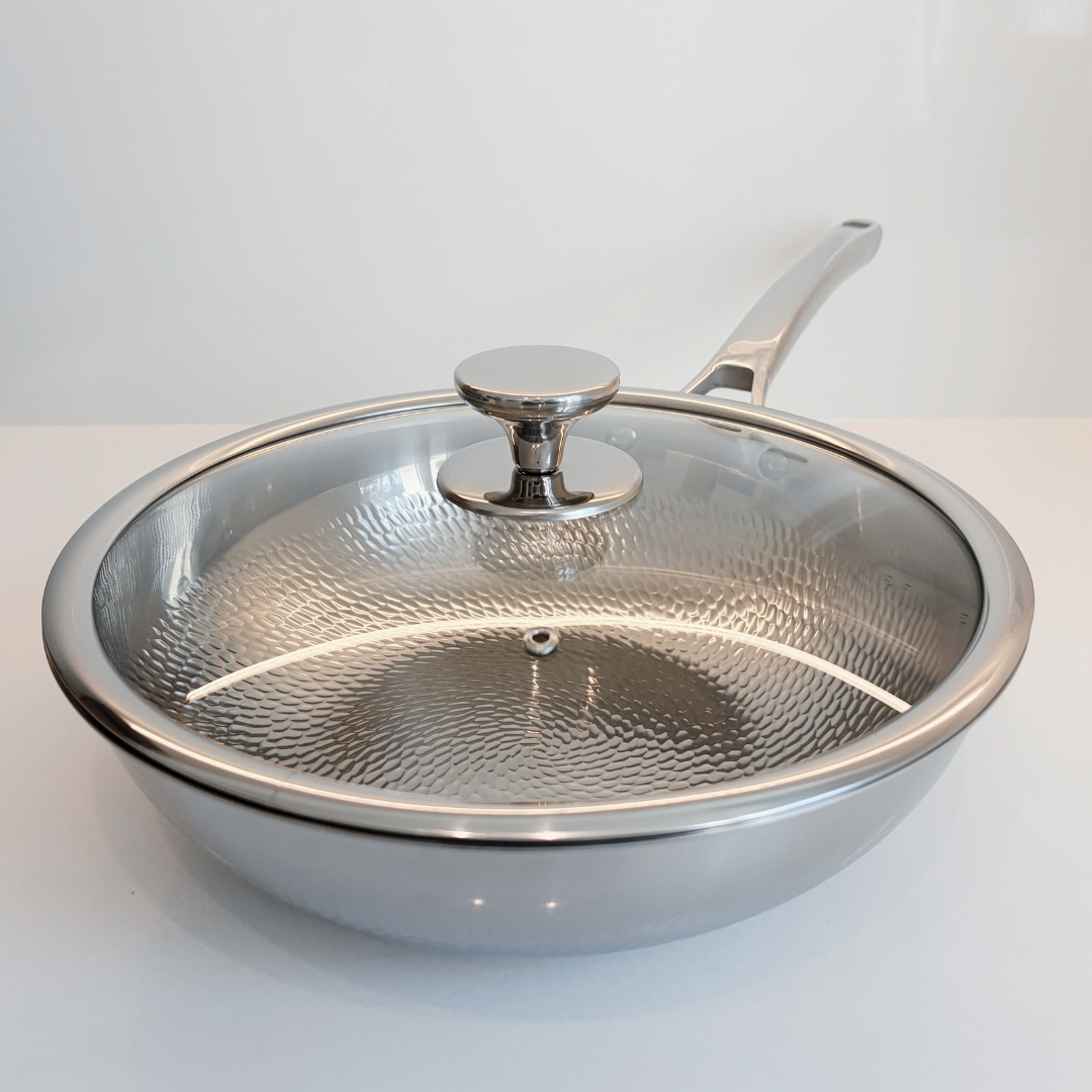 A Titanium sauté pan Wok with a clear glass lid featuring a hammered texture and a silver knob, set against a clean white background.