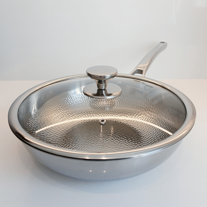 A Titanium sauté pan Wok with a clear glass lid featuring a hammered texture and a silver knob, set against a clean white background.