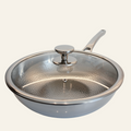 A titanium wok with a matching glass lid featuring a hammered texture and a silver knob, set against a plain off-white background.