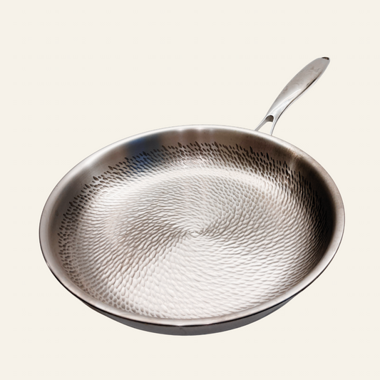 A hammered stainless steel frying pan with a long handle, shown from a top-down perspective on a light cream background.